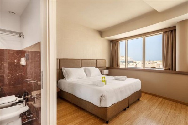 Nowoczesny pokój hotelowy z dużym łóżkiem i bocznym widokiem na łazienkę.