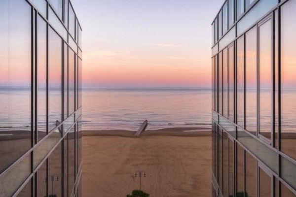 Widok między nowoczesnymi budynkami na plażę i morze o zachodzie słońca.