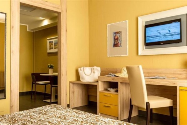 Pokój hotelowy z biurkiem, krzesłem i telewizorem na żółtej ścianie.