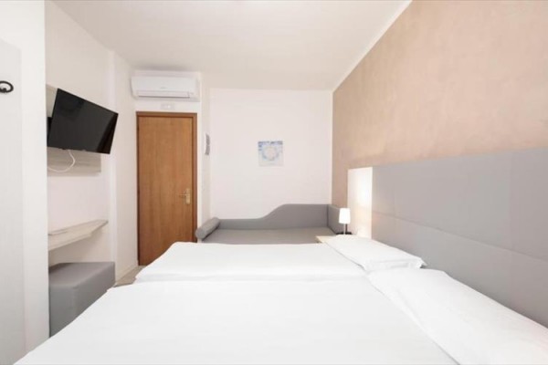 Nowocześnie urządzony pokój hotelowy z łóżkiem podwójnym, sofą i telewizorem na ścianie.