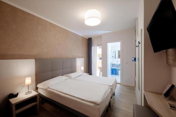 Nowoczesny pokój hotelowy z podwójnym łóżkiem, stolikami nocnymi i telewizorem na ścianie.
