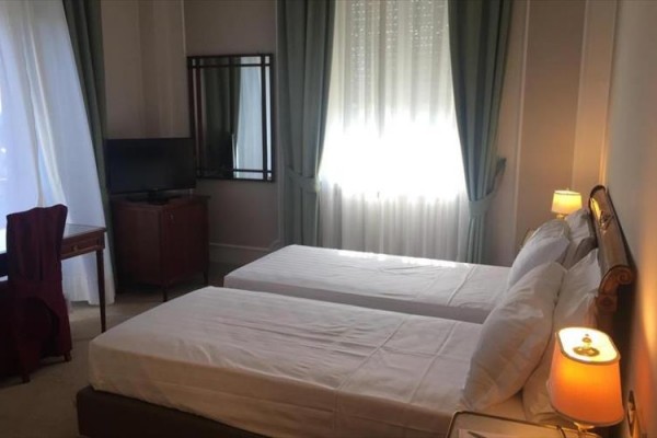 Pokój hotelowy z dwoma oddzielnymi łóżkami, biurkiem i telewizorem.