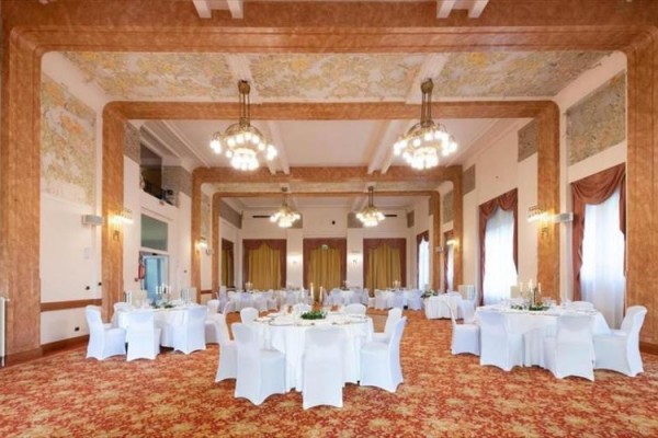 Przestronna sala bankietowa z okrągłymi stołami i krzesłami z białymi pokrowcami.