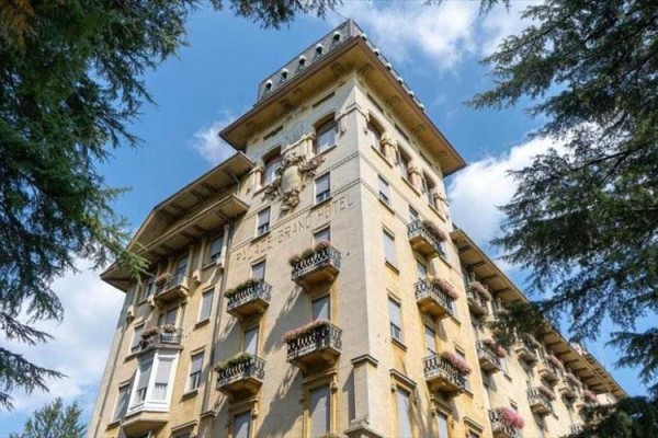 Zabytkowy budynek hotelu z balkonami i ozdobnymi detalami pod niebieskim niebem wśród drzew.