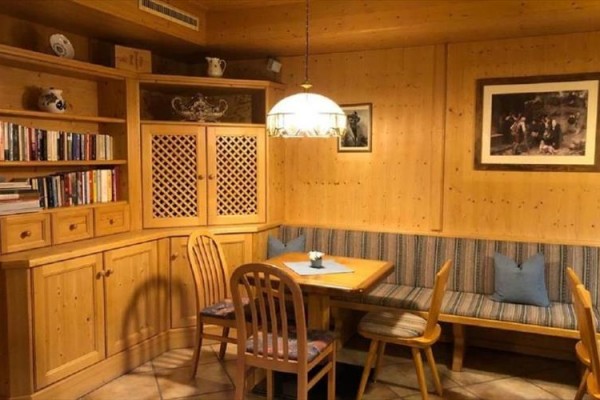 Drewniane wnętrze z wbudowanymi półkami, ławką, stołem i krzesłami, oświetlone lampą wiszącą.