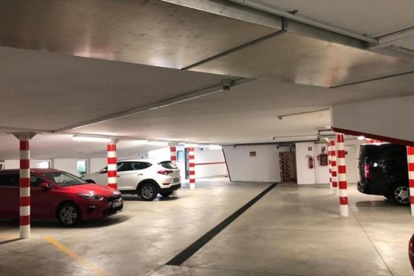 Podziemny parking z kilkoma zaparkowanymi samochodami i słupami w biało-czerwone paski.