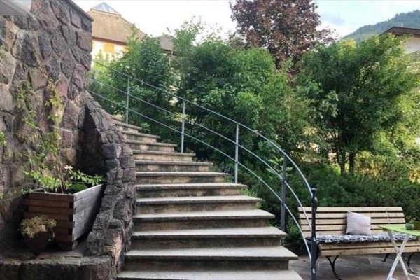 Zewnętrzne kamienne schody z metalową poręczą obok ławki i zieleni.