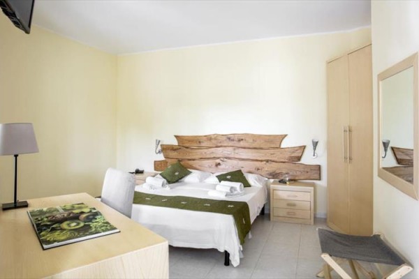 Nowoczesny pokój hotelowy z łóżkiem małżeńskim i drewnianym zagłówkiem.