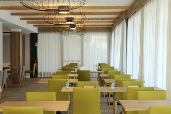Nowoczesna restauracja z drewnianymi stołami i zielonymi krzesłami.