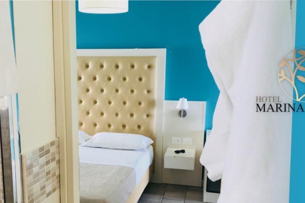 Pokój z niebieską ścianą, łóżkiem z tapicerowanym zagłówkiem oraz logo hotelu Marina del Capo.