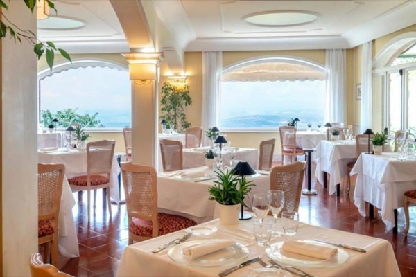 Elegancka restauracja z białymi obrusami i widokiem na morze przez duże okna.