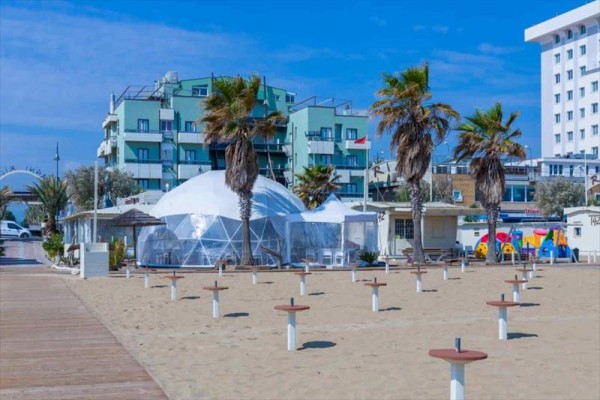 Plaża z palmami i nowoczesnymi budynkami w tle.