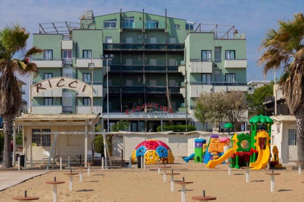 Plac zabaw na plaży z kolorowymi drabinkami i zielonym budynkiem w tle.
