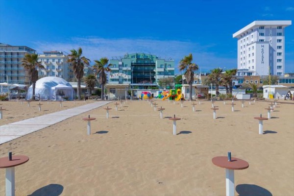 Piaszczysta plaża z parasolami, palmami i hotelami w tle.