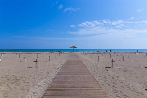 Drewniana ścieżka na piaszczystej plaży kończy się przy parasolu, w tle morze.