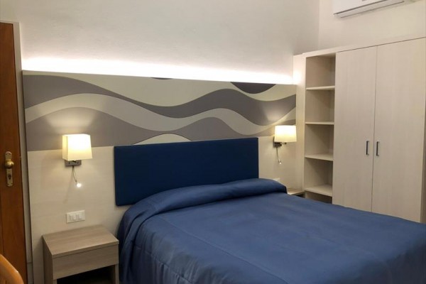 Pokój hotelowy z łóżkiem pokrytym niebieską pościelą i falistą tapetą na ścianie.