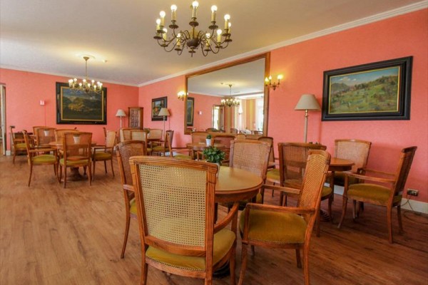 Restauracja z drewnianymi stołami i krzesłami, różowymi ścianami i żyrandolami.