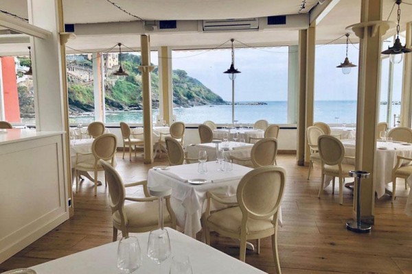 Restauracja z białymi stołami i widokiem na morze i wybrzeże.