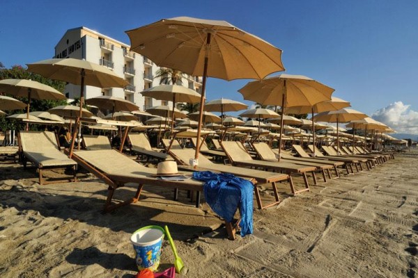 Rząd leżaków z brązowymi parasolami na piaszczystej plaży obok hotelu.