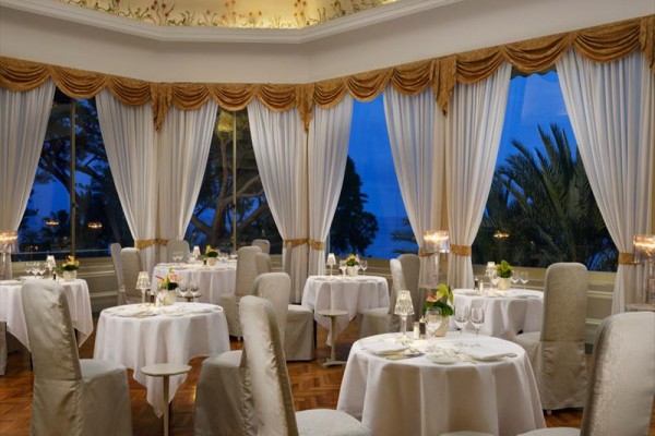 Elegancka restauracja z okrągłymi stolikami i dużymi oknami z widokiem na zewnętrzny krajobraz.