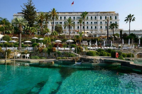 Zabytkowy hotel z basenem i ogrodem otoczonym palmami.