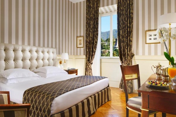 Elegancki pokój hotelowy z dużym łóżkiem, widokiem z okna i dekoracjami w brązowych tonacjach.