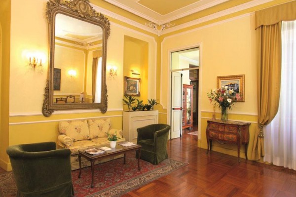 Elegancki salon z kremowymi ścianami, dużym lustrem i zabytkowymi meblami.  