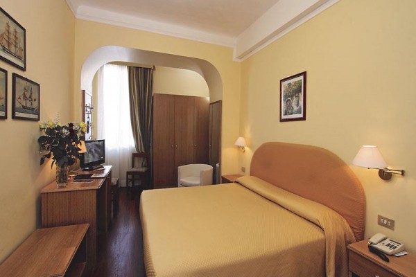 Pokój hotelowy z łóżkiem małżeńskim, telewizorem i szafą obok okna z ciemną zasłoną.