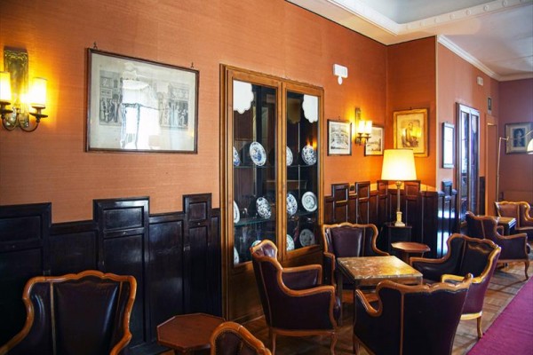 Elegancki salon z skórzanymi fotelami, drewnianymi panelami i witryną z porcelaną.