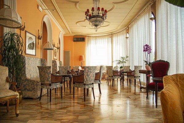 Eleganckie wnętrze z fotelami i zasłonami, oświetlone żyrandolami.