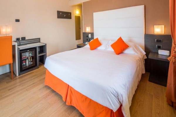 Pokój hotelowy z dużym łóżkiem, pomarańczowymi poduszkami i zasłonami.