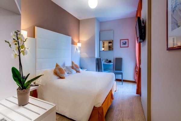 Pokój hotelowy z łóżkiem małżeńskim, biurkiem i kwiatem na stole.