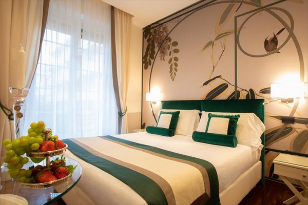 Elegancki pokój hotelowy z dużym łóżkiem i dekoracyjnymi owocami na stole.