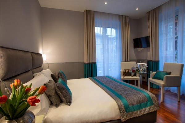 Nowoczesny pokój hotelowy z łóżkiem małżeńskim, fotelami i telewizorem na ścianie.