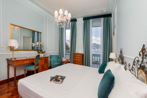 Elegancki pokój hotelowy z dużym łóżkiem, biurkiem i balkonem z widokiem na góry.