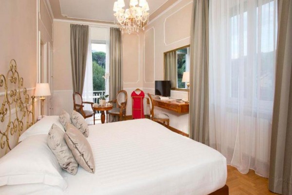 Elegancki pokój hotelowy z dużym łóżkiem, fotelami i widokiem na zieleń.