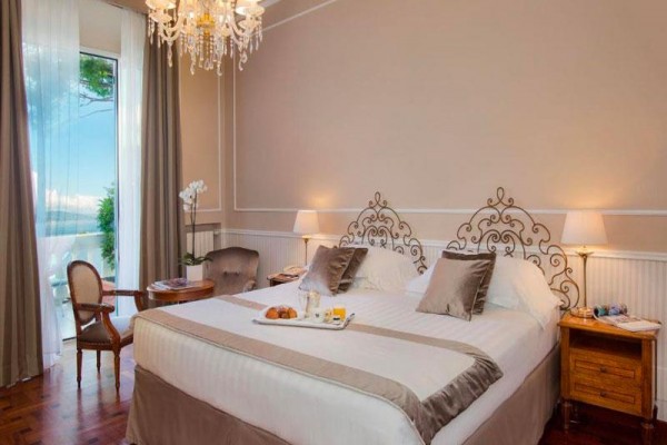 Luksusowy pokój hotelowy z podwójnym łóżkiem, żyrandolem i balkonem z widokiem na morze.
