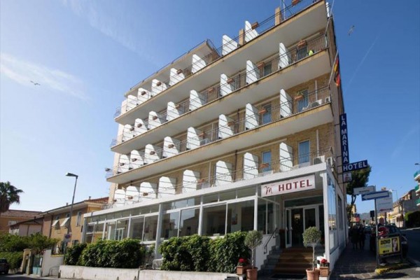 Czteropiętrowy hotel z balkonami i wejściem od ulicy.