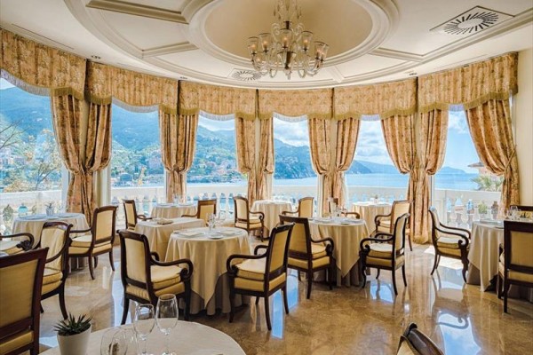 Elegancka restauracja z okrągłymi stołami i widokiem na morze i góry.