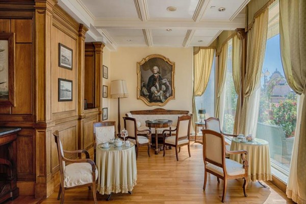 Elegancka kawiarnia z drewnianą boazerią, zabytkowymi meblami i obrazem mężczyzny na ścianie.