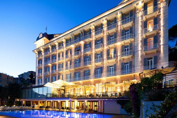 Luksusowy hotel z oświetloną fasadą i odkrytym basenem o zmierzchu.