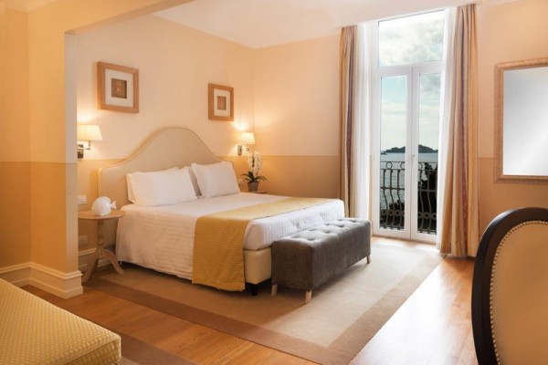 Elegancki pokój hotelowy z dużym łóżkiem i widokiem na morze z balkonu.