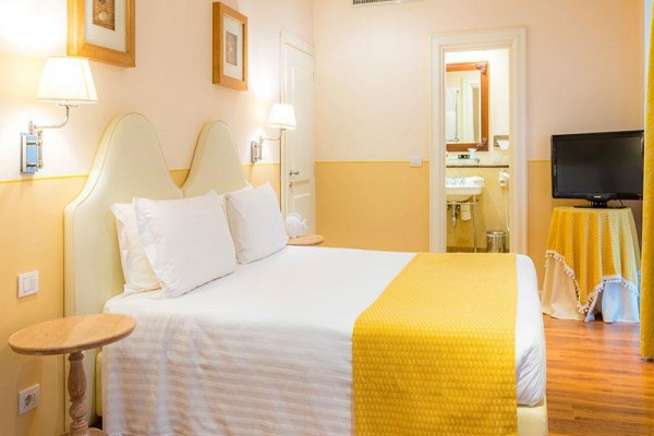 Pokój hotelowy z podwójnym łóżkiem, żółtymi dodatkami i przyległą łazienką.