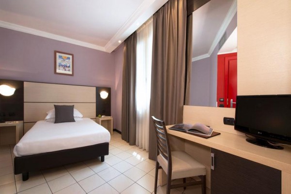 Nowoczesny pokój hotelowy z pojedynczym łóżkiem, biurkiem i telewizorem.