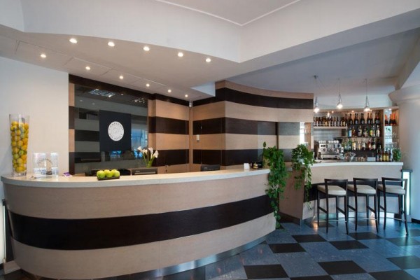 Nowoczesna recepcja hotelowa z drewnianym wykończeniem i barem w tle.