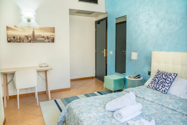 Pokój hotelowy z niebieską ścianą, łóżkiem, biurkiem i obrazem na ścianie.