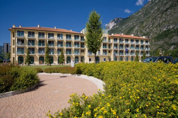 Budynek hotelu z balkonami otoczony górami i zielenią.