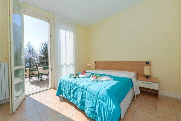 Jasna sypialnia z łóżkiem i otwartymi drzwiami na balkon.