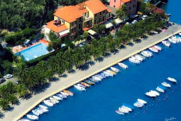 Hotel z basenem przy promenadzie nadmorskiej otoczonej palmami i łodziami.