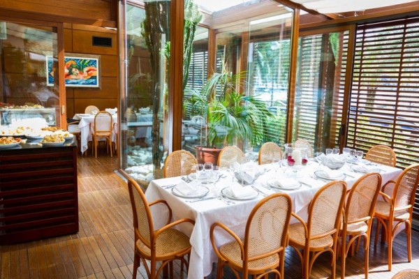 Elegancko nakryty stół w przeszklonej restauracji z rattanowymi krzesłami i widokiem na zieleń.